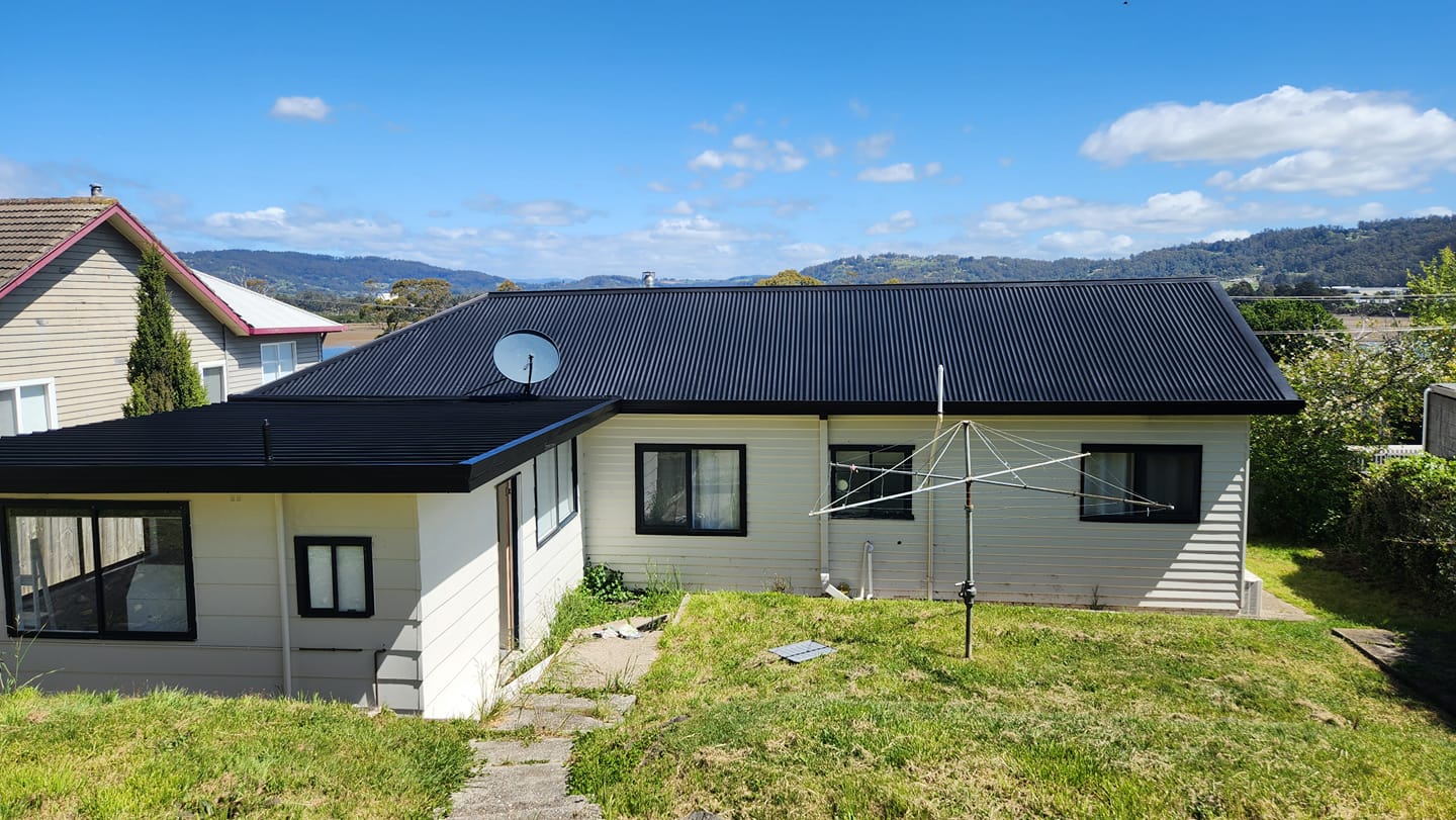 White weatherboard home with fresh black metal roof, Tassie hills behind