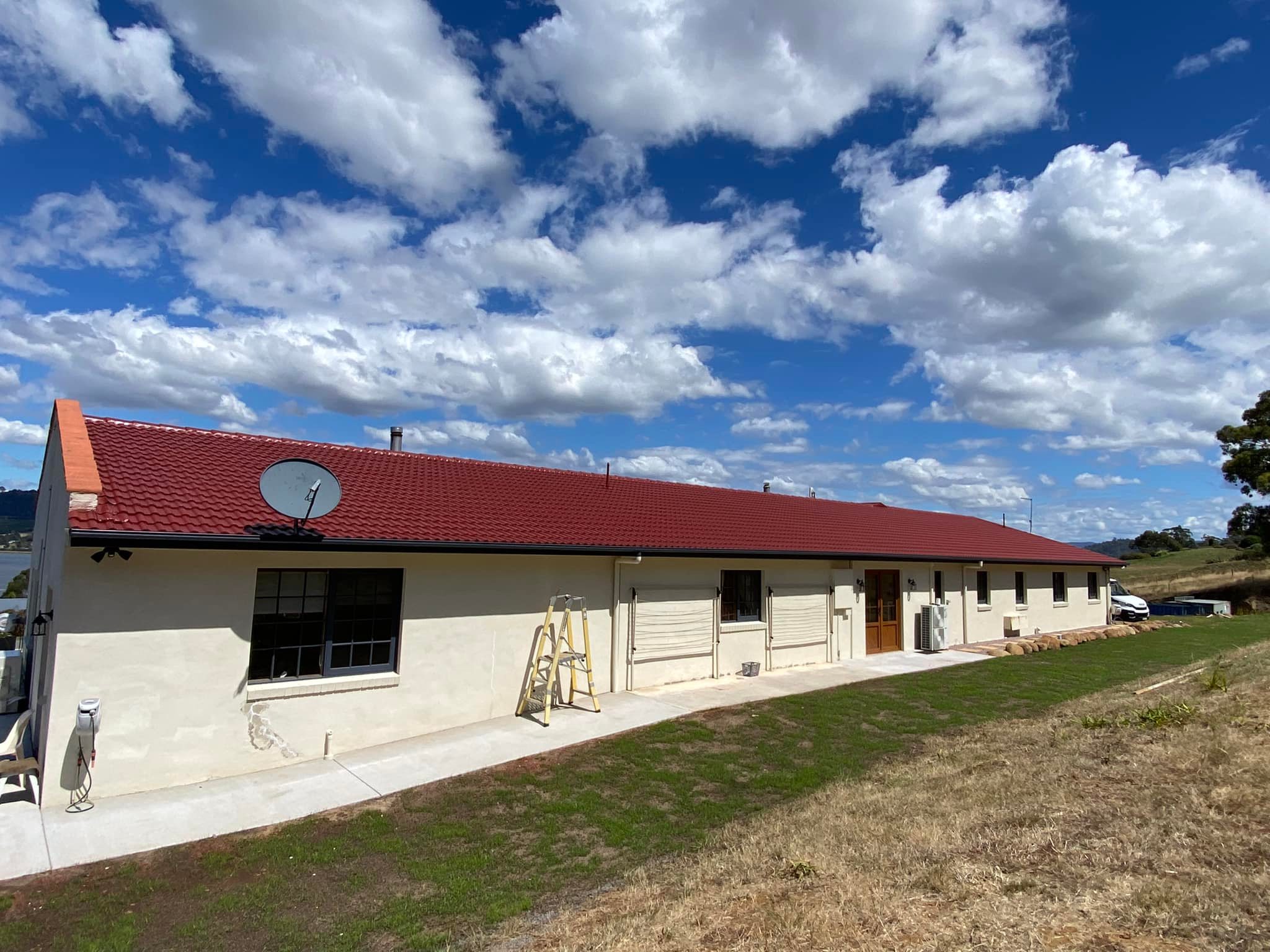 Long farm home with bright cherry-red tile roof and Tassie clouds